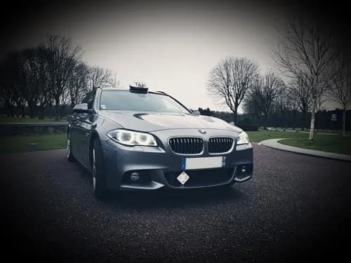 Taxi à Arras, votre taxi conventionné haut de gamme Pas-de-Calais Hauts-de-France Taxi BMW noir vu de trois quarts avant, phares allumés.
