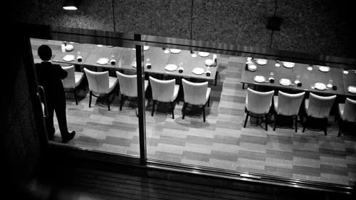Transport sécurisé Hauts de France avec chauffeur privé diplômé sécurité Vue en noir et blanc d’une salle de restaurant avec de longues tables dressées et un homme au premier plan.