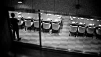 Transport sécurisé Hauts de France avec chauffeur privé diplômé sécurité Vue en noir et blanc d’une salle de restaurant avec de longues tables dressées et un homme au premier plan.